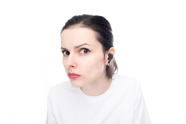 эмоциональная женщина в белой футболке с маленьким наушником в ухе на белом студийном фоне