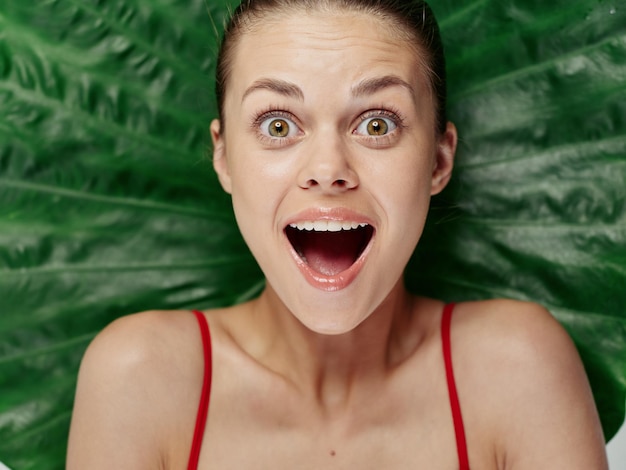 Photo emotional woman with open mouth with bare shoulders palm leaf on background high quality photo