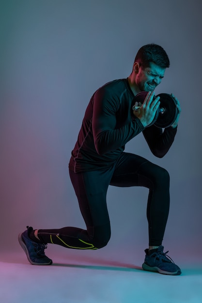 Emotional young athletic man doing lunges with dumbbell