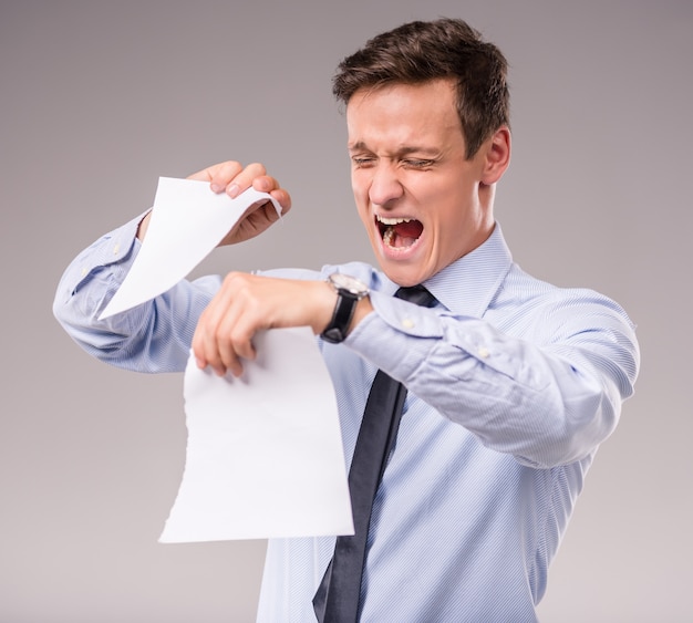 Emotional young businessman tearing paper.