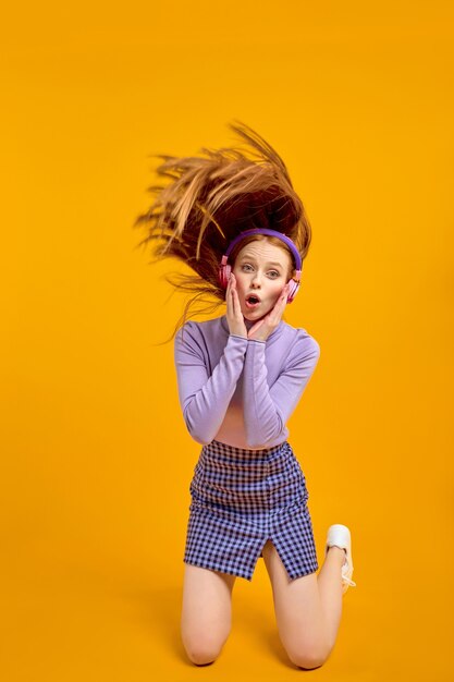 Emotional young happy crazy woman in headphones with flying hair isolated on yellow color background...