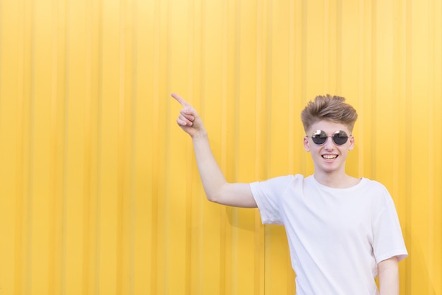 An emotional young man stands on an orange wall and shows his hands aside to the place for the text. Copyspace