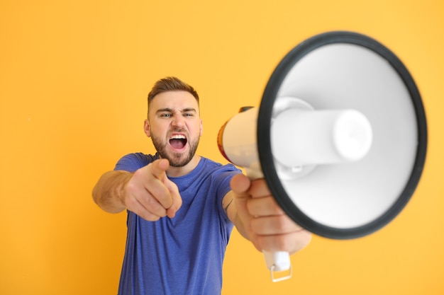 Emotional young man with megaphone on orange