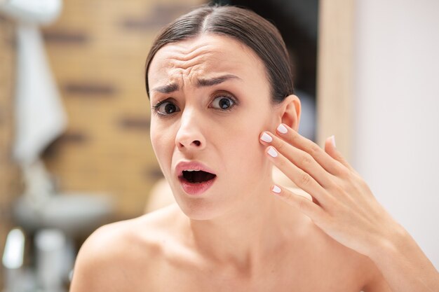 Emotional young woman looking scared and opening her mouth while touching the cheek