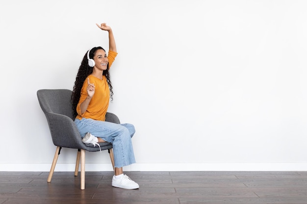 Emotional young woman sitting at arm chair listening to\
music