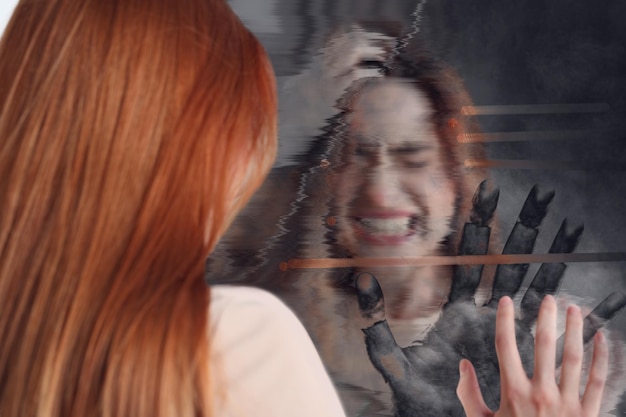 Foto giovane donna emotiva che soffre di allucinazioni che tocca lo specchio rotto sul retro con l'effetto glitch