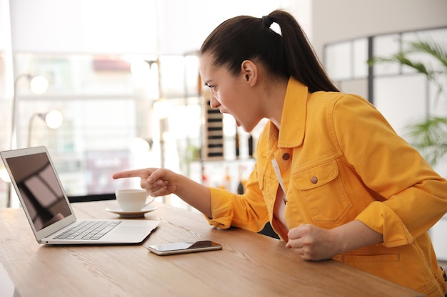 Emotional young woman working on laptop in office Online hate concept