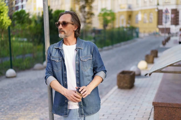 Emotionally exhausted middle age crisis mature man leaned on road sign holding paper cup off coffee Experiencing hangover middle age alcoholic man drink using paper cup to hide alcohol