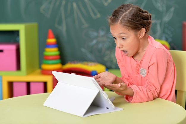 Emotioneel meisje dat tablet met schoolbord op achtergrond gebruikt