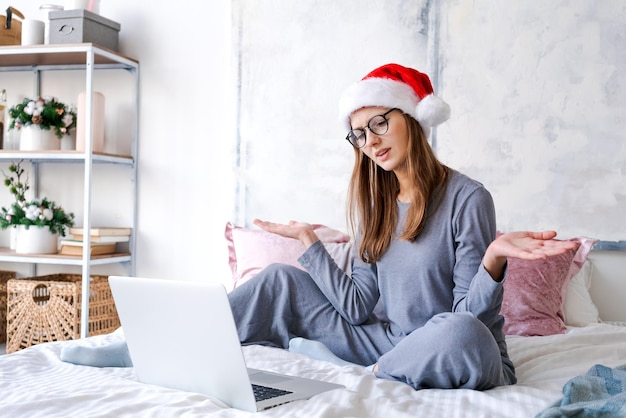 Emotioneel meisje dat thuis zit met laptop in kerstmuts, gebaren met haar