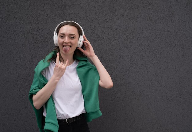 Emotioneel meisje luistert naar muziek in koptelefoon op een grijze achtergrond toont tong en heavy metal