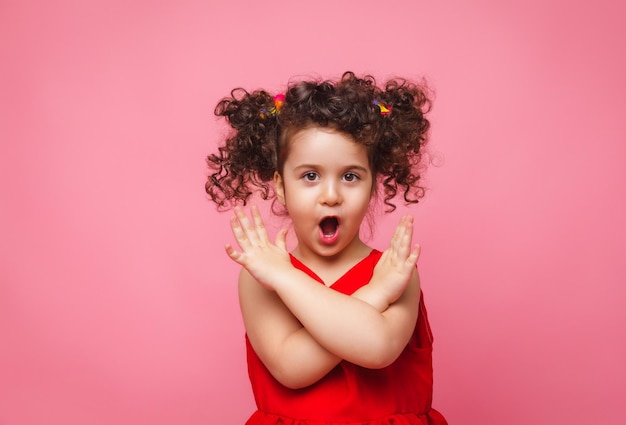 Emotioneel portret van een klein meisje in een rode jurk op een roze achtergrond