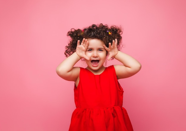 Emotioneel portret van een klein meisje in een rode jurk op een roze achtergrond