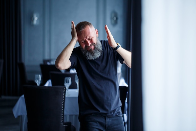 Emotioneel portret van een volwassen grijsharige man met een baard in een zwart t-shirt