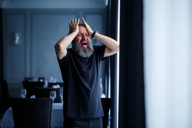 Emotioneel portret van een volwassen grijsharige man met een baard in een zwart t-shirt