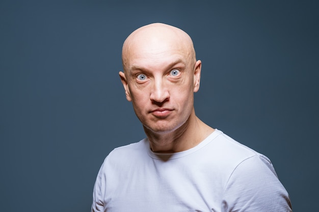 Emotioneel portret van een volwassen kale man in een witte t-shirt op een grijze close-up als achtergrond