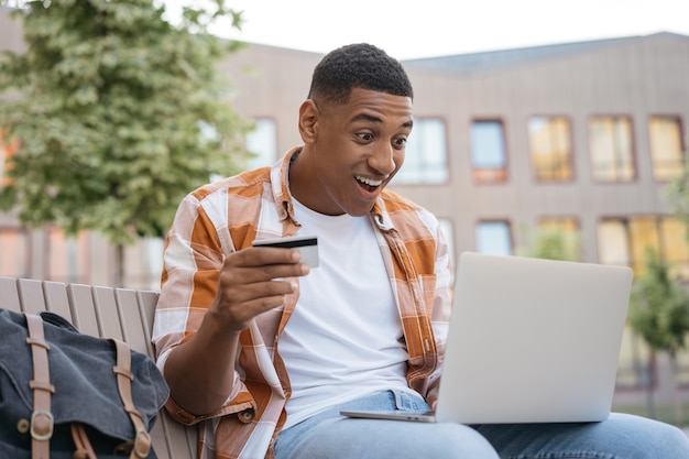 Emotionele Afro-Amerikaanse man met creditcard die online winkelt met grote verkopen op Black Friday