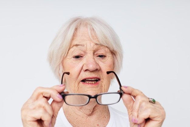 Emotionele bejaarde vrouw in casual t-shirt en glazen lichte achtergrond