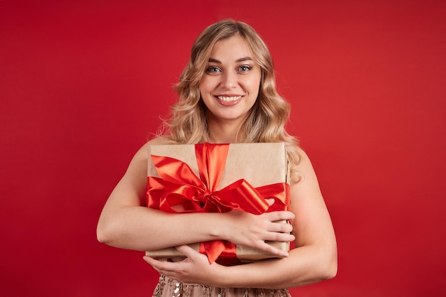 Emotionele blondine is blij met het geschenk kijkt naar de camera isolaat op een rode achtergrond gelukkig nieuw jaar...