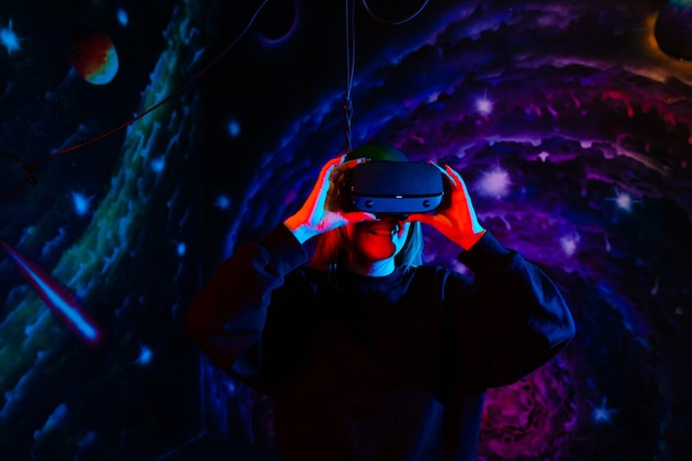 Emotionele gelukkig meisje in moderne virtual reality-bril met neon rood en blauw licht op de achtergrond van de ruimte in de speelkamer