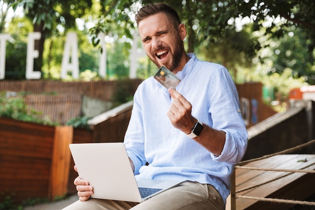 Emotionele jonge bebaarde man met creditcard.