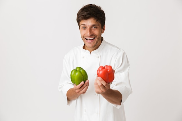 Emotionele jonge chef-kok geïsoleerd op witte paprika te houden.