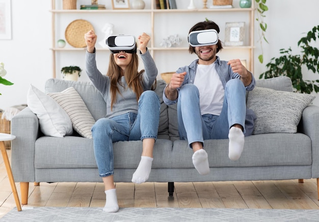 Emotionele jonge familie man en vrouw spelen videogames in de woonkamer thuis. VR-bril gebruiken en gebaren maken. Emotionele man en vrouw die moderne entertainmentapparatuur gebruiken, plezier hebben in het weekend