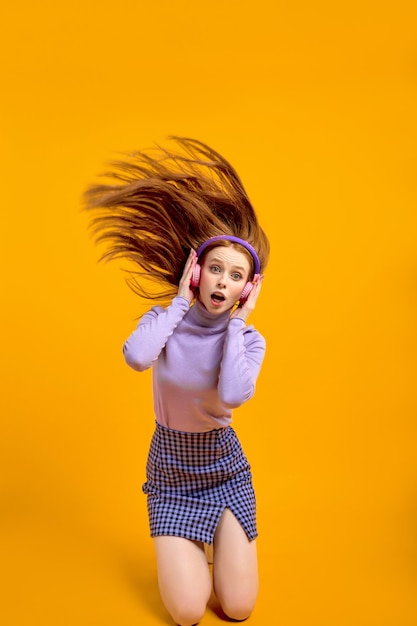 Emotionele jonge gelukkig gekke vrouw in koptelefoon met vliegende haren geïsoleerd op gele kleur achtergrond...