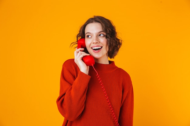 emotionele jonge mooie vrouw poseren geïsoleerd op gele muur praten via de telefoon.