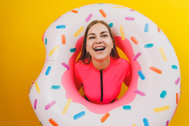 Emotionele jonge vrouw draagt een roze zwempak met een opblaasbare ring geïsoleerd op een felgele achtergrond Zomer hotel zwembad zee vakantie zon bruiningsconcept