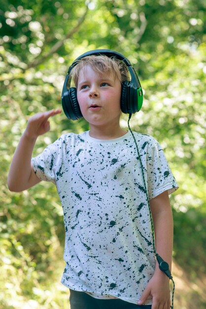 Emotionele jongen 9 jaar oud in het bos met koptelefoon luisteren naar muziek