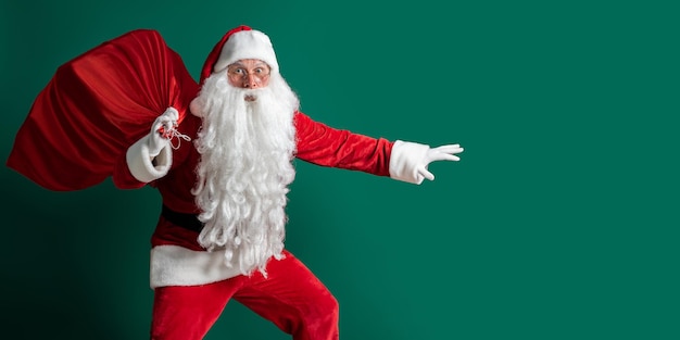 Emotionele kerstman sluipt terwijl hij een grote rode zak draagt met cadeautjes op een groene studioachtergrond