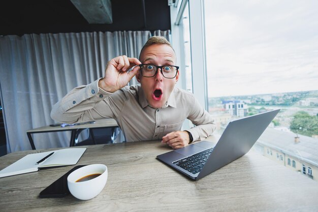 Emotionele man kijkt naar de camera op de werkplek een man met een bril zit op een desktop met een computer een student is op zoek naar inspiratie voor nieuwe ideeën in een kantoorcafé