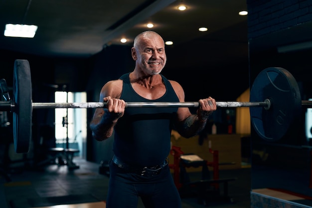 emotionele oudere kale bodybuilder traint in de sportschool terwijl hij zijn bicepsspieren oppompt met een halter