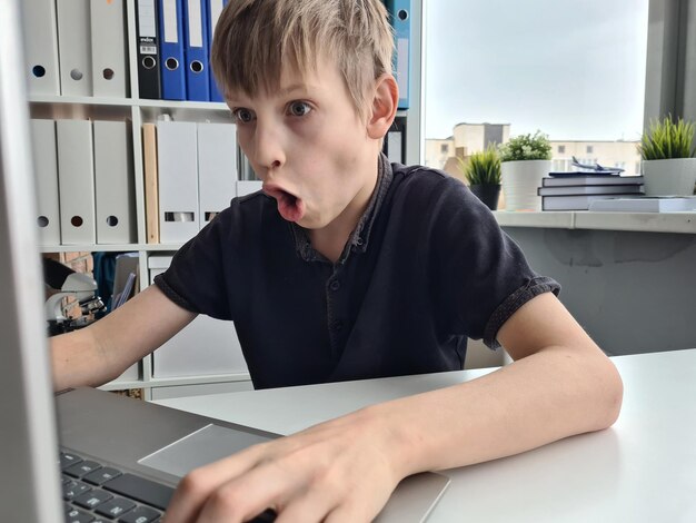 Emotionele slimme jongen kijkt geschokt en kijkt naar laptop