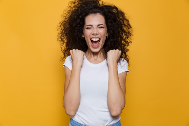 emotionele vrouw 20s met krullend haar schreeuwen en balde vuisten geïsoleerd op geel