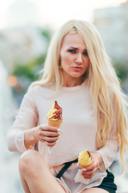 Emotionele vrouw, blond, met twee ijsjes poseren tegen de achtergrond van de stad.