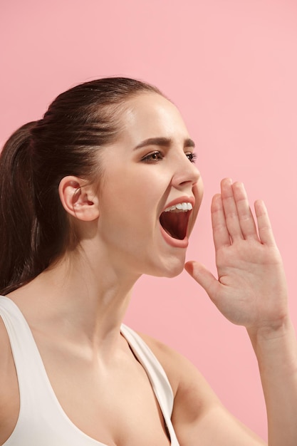 Emotionele vrouw die op roze muur schreeuwt