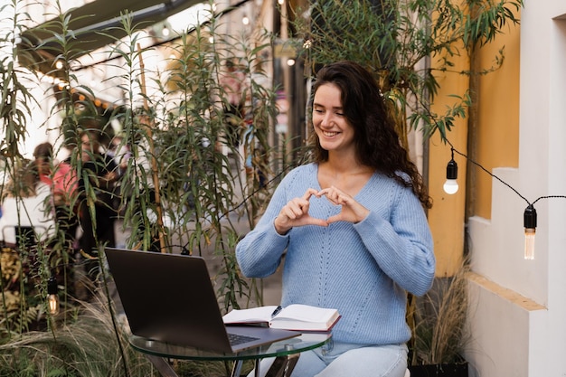 Emotionele vrouw lacht en communiceert met vrienden en heeft plezier via videoverbinding Vrolijk meisje met laptop grimassen en videochatten met vrienden en familie in café buiten