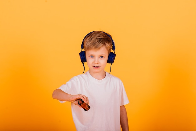 Emotions boy listens to music with headphones on his phone, yellow background. Children's fairy tales in headphones.