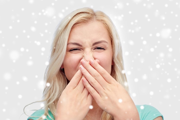 emotions, expressions, embarrassment, and people concept - young woman or teenage girl wrinkling and closing her nose of unpleasant smell over snow