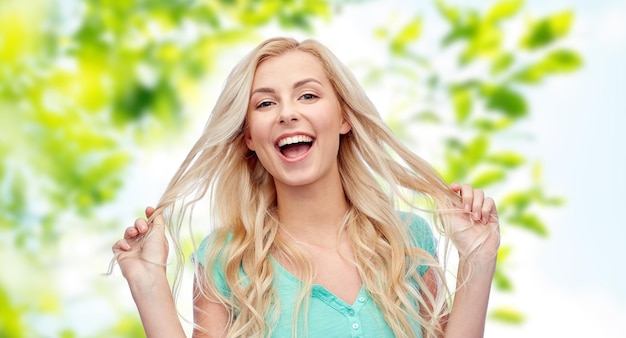 Photo emotions, expressions, hairstyle and people concept - smiling young woman or teenage girl holding her strand of hair over green natural background