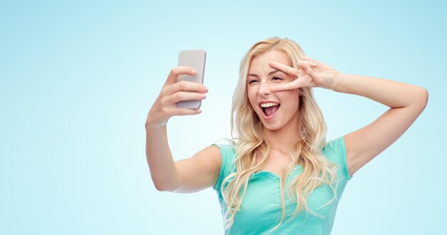 emotions, expressions and people concept - happy smiling young woman or teenage girl taking selfie with smartphone over blue background