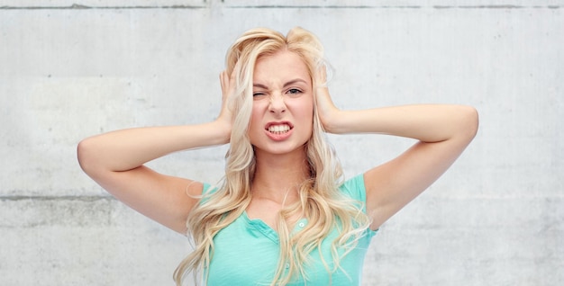 Photo emotions, expressions, stress and people concept - young woman holding to her head and screaming over gray concrete wall background