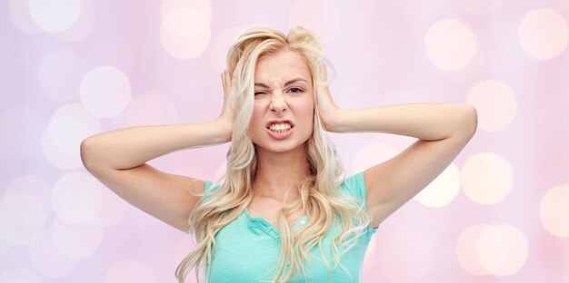 Foto emozioni, espressioni, stress e concetto di persone - giovane donna che si tiene alla testa e urla sullo sfondo delle luci delle vacanze rosa