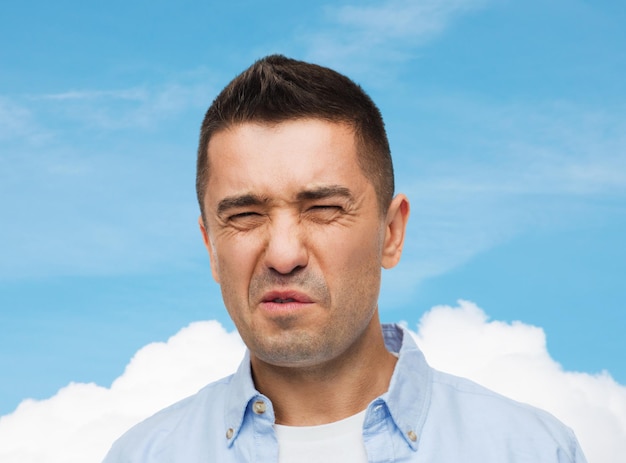 emotions, facial expression and people concept - man wrying of unpleasant smell over blue sky and cloud background