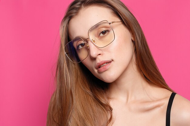 Emotions, fashion, people, youth and beauty concept - Close up shot of stylish young woman in sunglasses smiling against pink background. Beautiful female model with copy space.