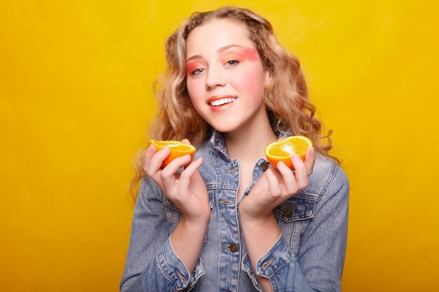 Emotions health people food and beauty concept beauty model girl takes juicy oranges beautiful joyful teen girl with freckles funny hairstyle yellow makeup professional make up orange slice