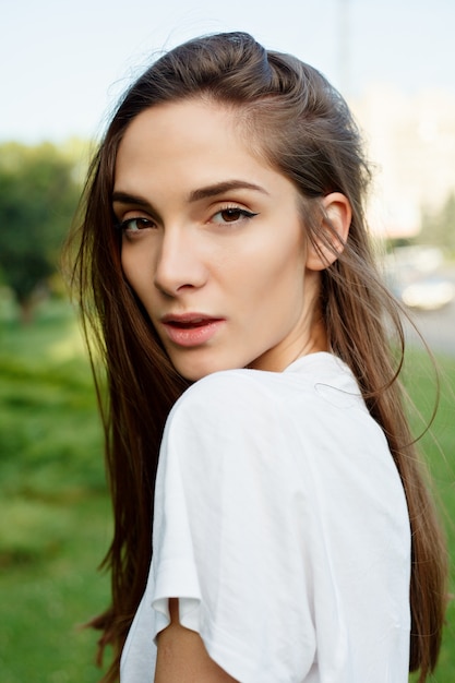 Emotions, lifestyle, beauty, people concept - Portrait of a young attractive brunette female in a white T-shirt on the waterfront and smiling on the sunset. than turns to camera and smiles