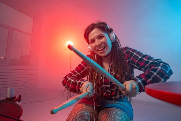 Emotions, music, hobbies and people concept - young woman playing the electronic drum set in studio